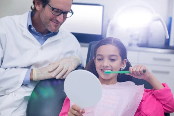 Dentista asistiendo a paciente joven mientras se cepilla los dientes —  Fotos de Stock