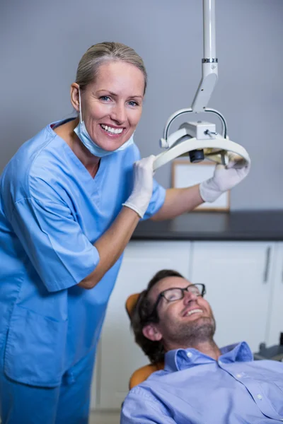 Smiling dentist assistant adjusting light over patients mouth — Stock Photo, Image