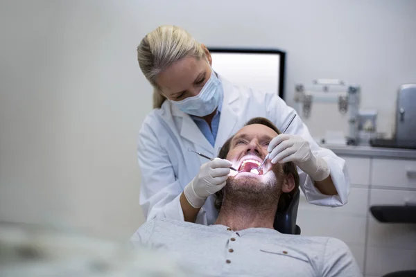 Dentista examinando a un paciente con herramientas — Foto de Stock