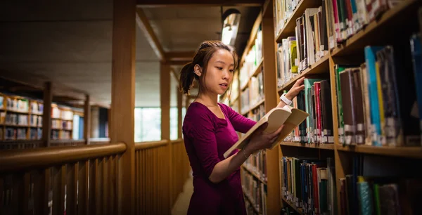 Jovem mulher selecionando livro na biblioteca — Fotografia de Stock