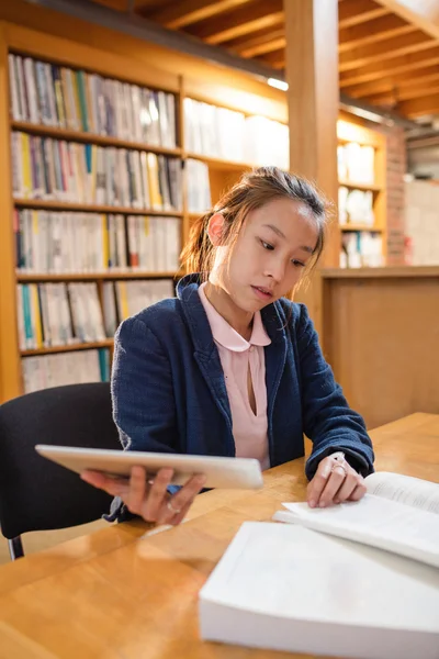 Mujer joven usando tableta digital mientras estudia en la biblioteca — Foto de Stock