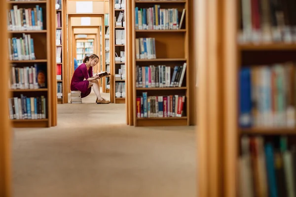 Jovem mulher lendo livro na biblioteca — Fotografia de Stock