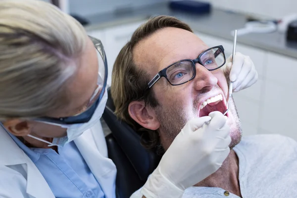 Kvinnliga tandläkare undersökande manlig patient med verktyg — Stockfoto