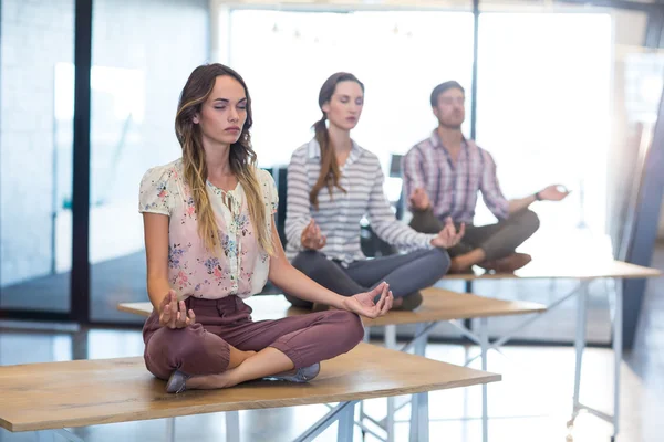 Business people performing yoga on table — Stock Photo, Image