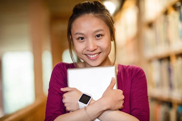 Mujer joven sosteniendo tableta digital en la biblioteca — Foto de Stock