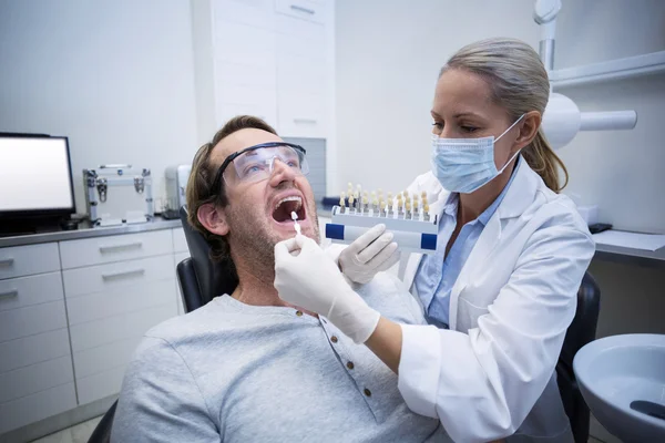 Female dentist examining male patient with teeth shades — Stock Photo, Image