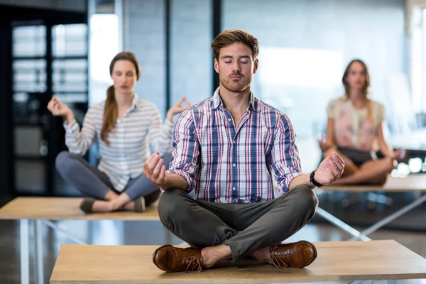 Business people performing yoga on table — Stock Photo, Image