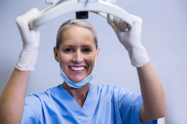 Asistente dental sonriente ajustando la luz en la clínica —  Fotos de Stock