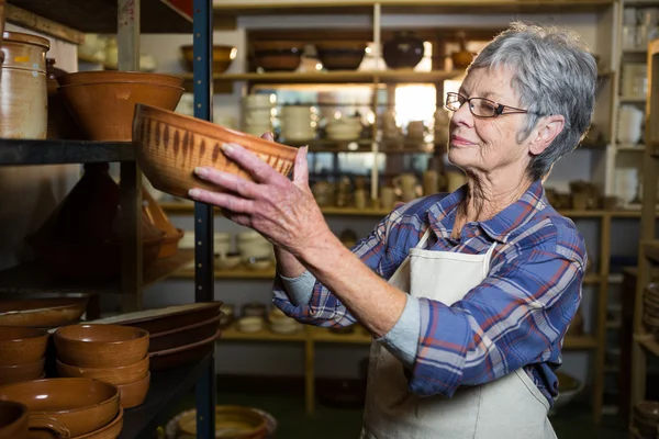 Female potter placing bowl on shelf — Stock Photo, Image