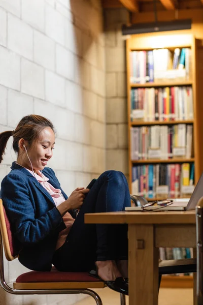 Ung kvinna med mobiltelefon i biblioteket — Stockfoto