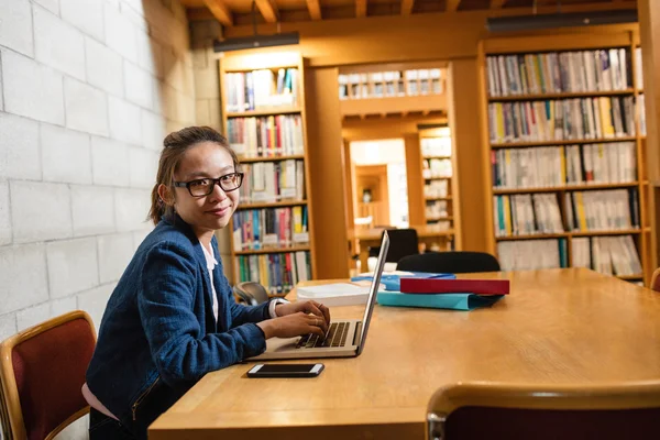 Mujer joven usando el ordenador portátil en la biblioteca — Foto de Stock