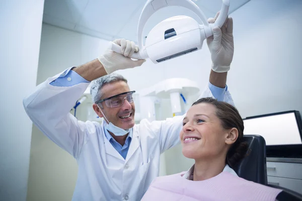 Dentista femenina ajustando la luz dental sobre el paciente —  Fotos de Stock