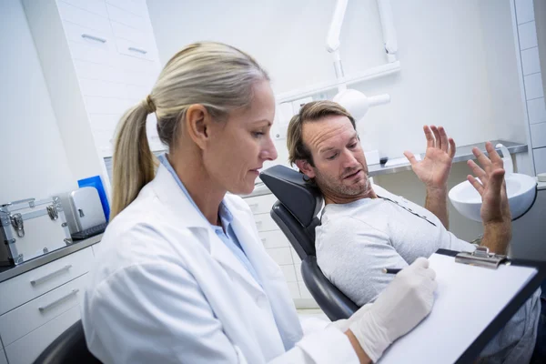 Zahnärztin schreibt auf Klemmbrett, während sie mit Mann interagiert — Stockfoto