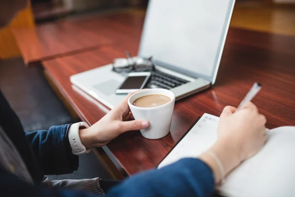 Woman writing in book while having tea — Stock Photo, Image