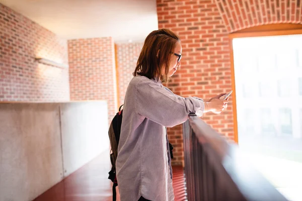 Jeune femme utilisant un téléphone portable dans le couloir — Photo