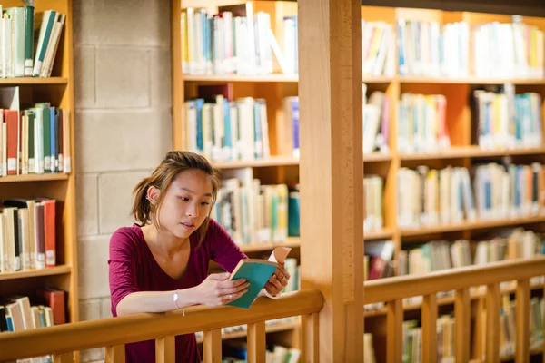 Giovane donna che legge libro in biblioteca — Foto Stock