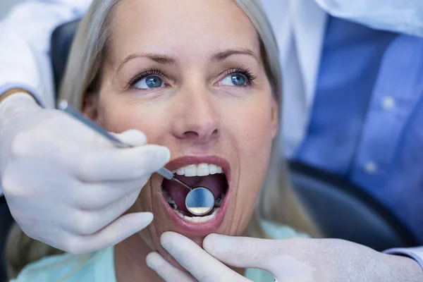 Dentista examinando a una mujer con herramientas — Foto de Stock