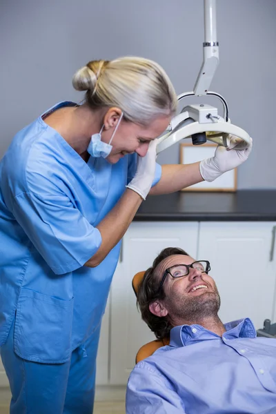 Assistente de dentista sorridente ajustando a luz sobre a boca dos pacientes — Fotografia de Stock