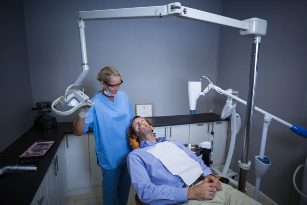 Assistant dentiste souriant ajustant la lumière sur la bouche des patients — Photo