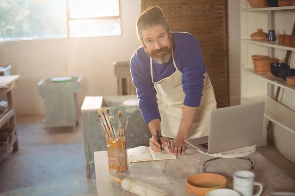 Male potter writing on a book — Stock Photo, Image