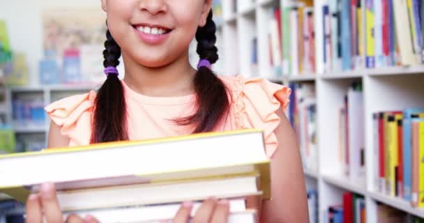 Schoolmeisje die stapel boeken in bibliotheek — Stockvideo