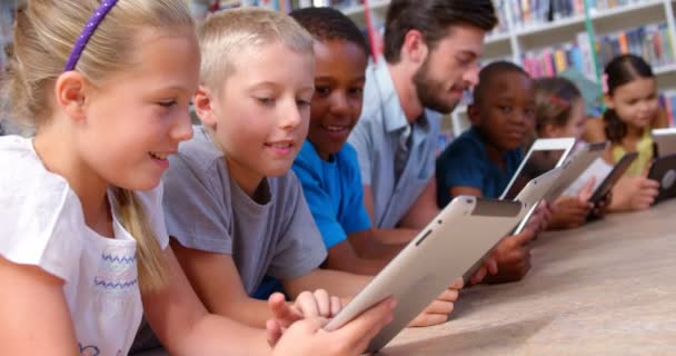 Crianças e professores usando tablet digital na biblioteca — Vídeo de Stock