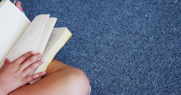 Schoolgirl sitting on floor and reading book — Stock Video