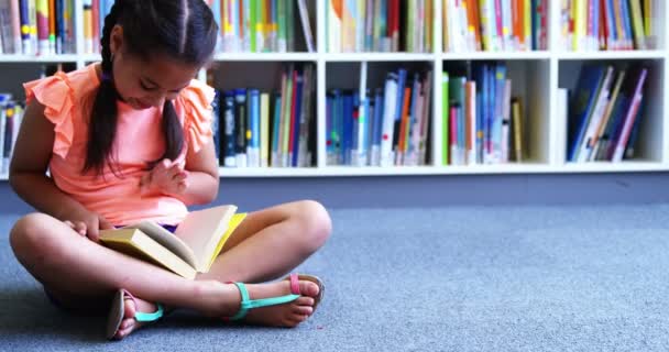 Школьница сидит на полу и читает книгу — стоковое видео