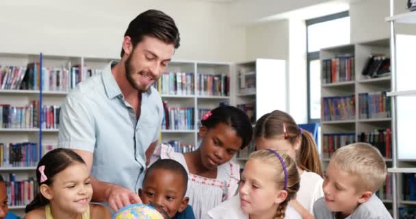 Profesor discutiendo globo con niños en la biblioteca — Vídeo de stock