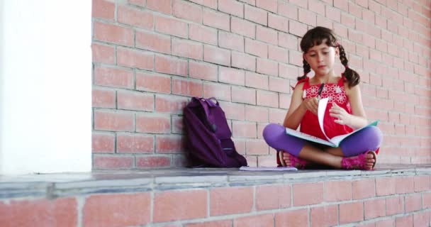 Girl sitting in corridor and doing homework — Stock Video