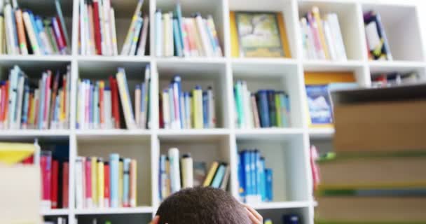 Schooljongen lezing boek in de bibliotheek op school — Stockvideo