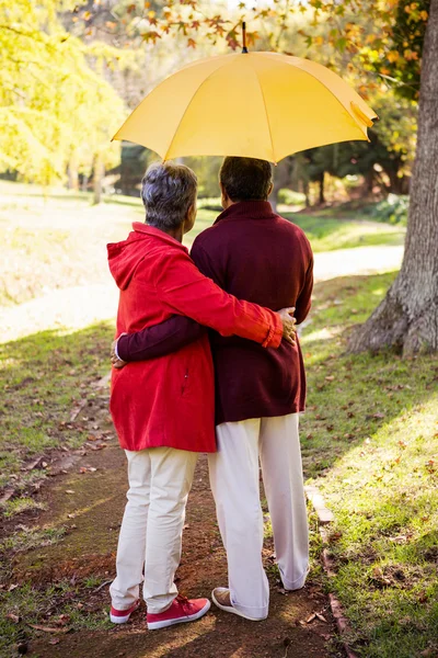 Casal segurando guarda-chuva ao abraçar — Fotografia de Stock