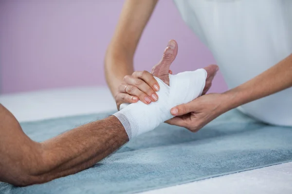 Physiotherapist putting bandage on injured hand of patient — Stock Photo, Image