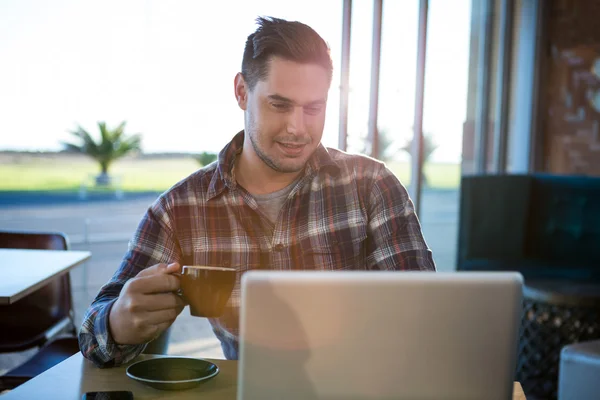 Smiling man using laptop while having coffee — Stock Photo, Image