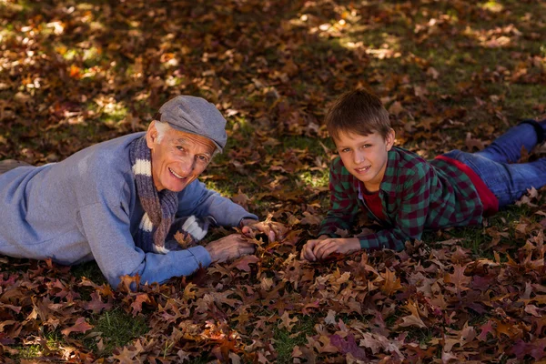 Dědeček a vnuk ležící na podzimní listí — Stock fotografie