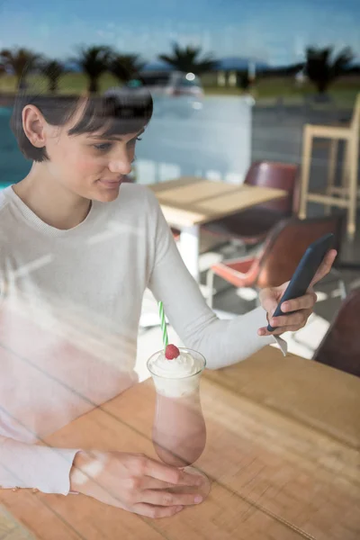 Mujer usando teléfono móvil mientras toma batido — Foto de Stock