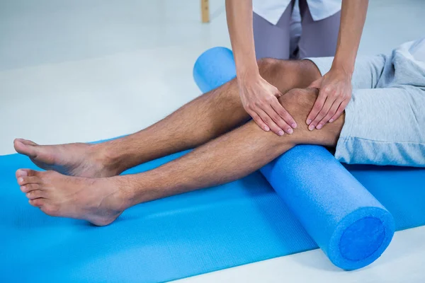 Fisioterapeuta fazendo terapia de perna para um homem usando rolo de espuma — Fotografia de Stock