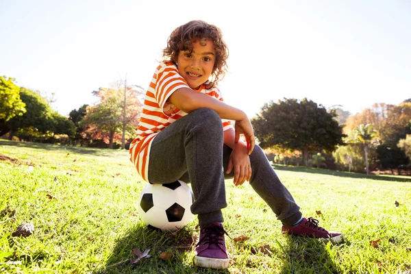 Niño sonriente sentado en la pelota de fútbol —  Fotos de Stock