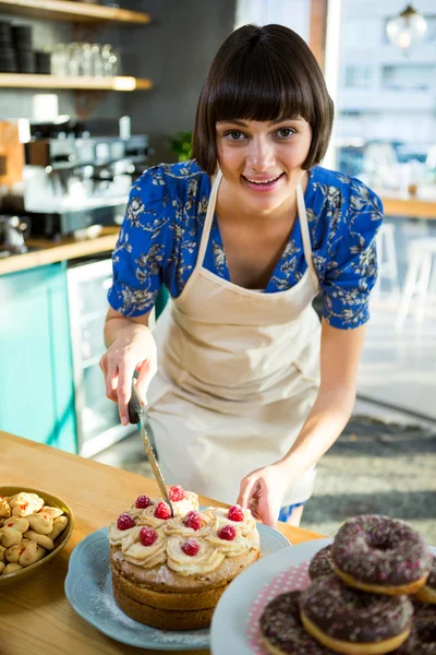 Leende servitris skära en tårta i kaféet — Stockfoto