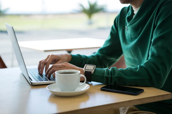 Kahve fincanı ve masa üstünde hareket eden telefon ile dizüstü bilgisayar kullanan adam — Stok fotoğraf