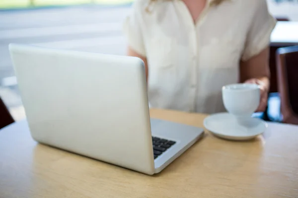 女人拿着一杯咖啡和使用笔记本电脑 — 图库照片