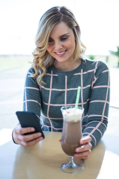 Vrouw met behulp van mobiele telefoon terwijl het hebben van milkshake — Stockfoto