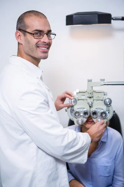 Optometrista sonriente examinando paciente femenina en phoropter —  Fotos de Stock