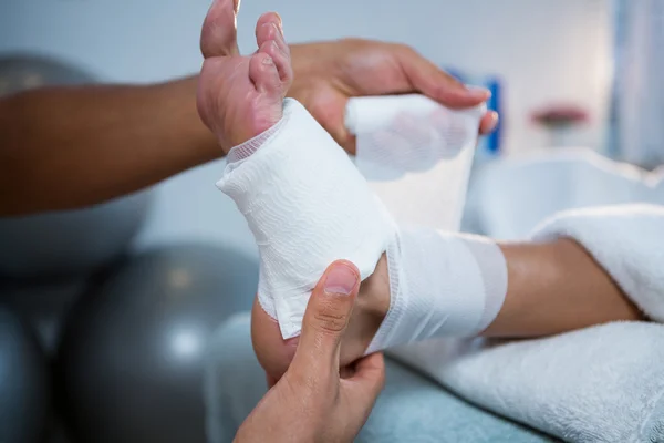 Physiotherapist putting bandage on injured feet of patient — Stock Photo, Image