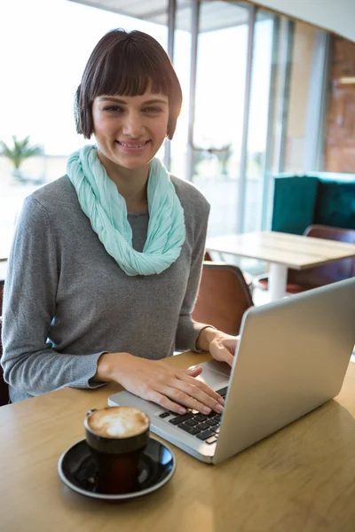 Mujer sonriente usando el ordenador portátil mientras toma café —  Fotos de Stock