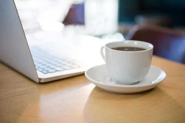 Zamknij - up filiżankę kawy i laptop na stole — Zdjęcie stockowe