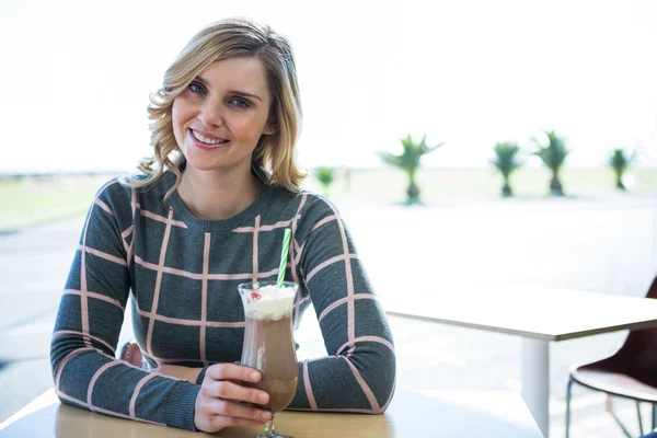 Mujer sonriente sentada en la cafetería y tomando batido —  Fotos de Stock