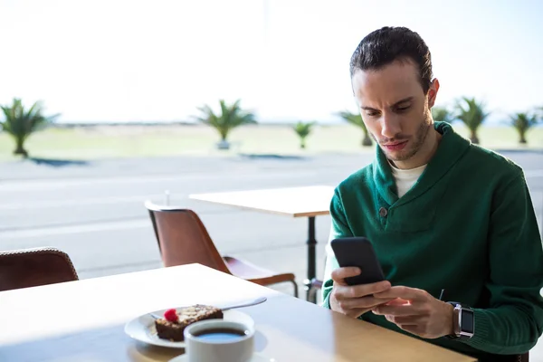 Hombre usando el teléfono móvil con pastel y taza de café en la mesa — Foto de Stock