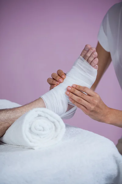 Fisioterapeuta poniendo vendaje en los pies lesionados del paciente — Foto de Stock