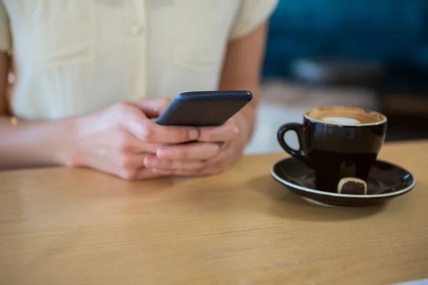 Vrouw met behulp van mobiele telefoon met koffiekopje op tafel — Stockfoto